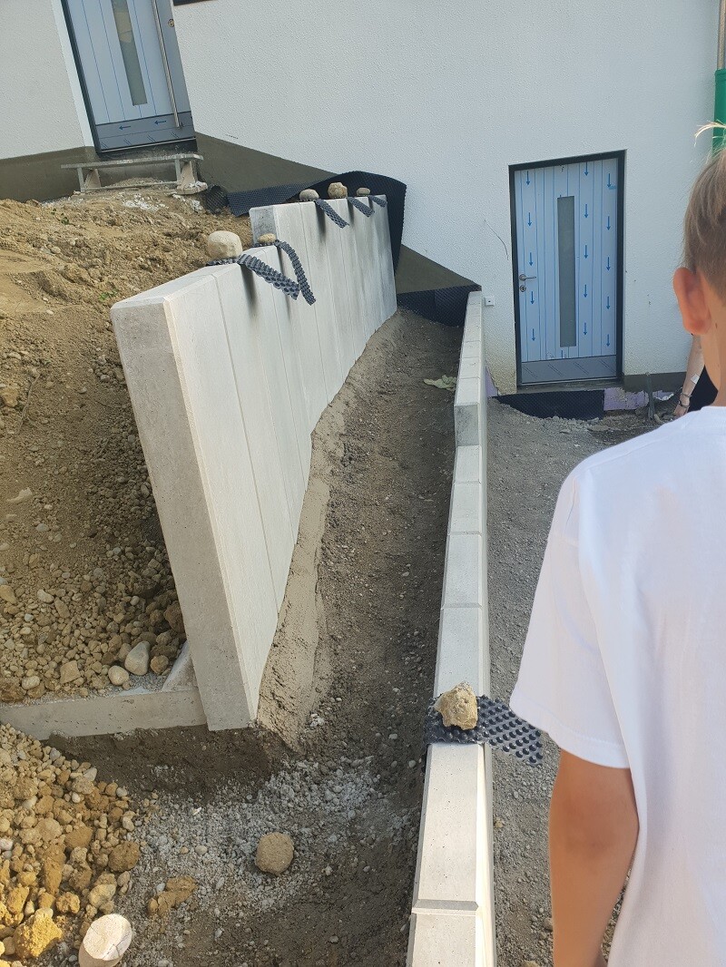 Construction site with concrete retaining wall, basement door and excavation work, person in foreground