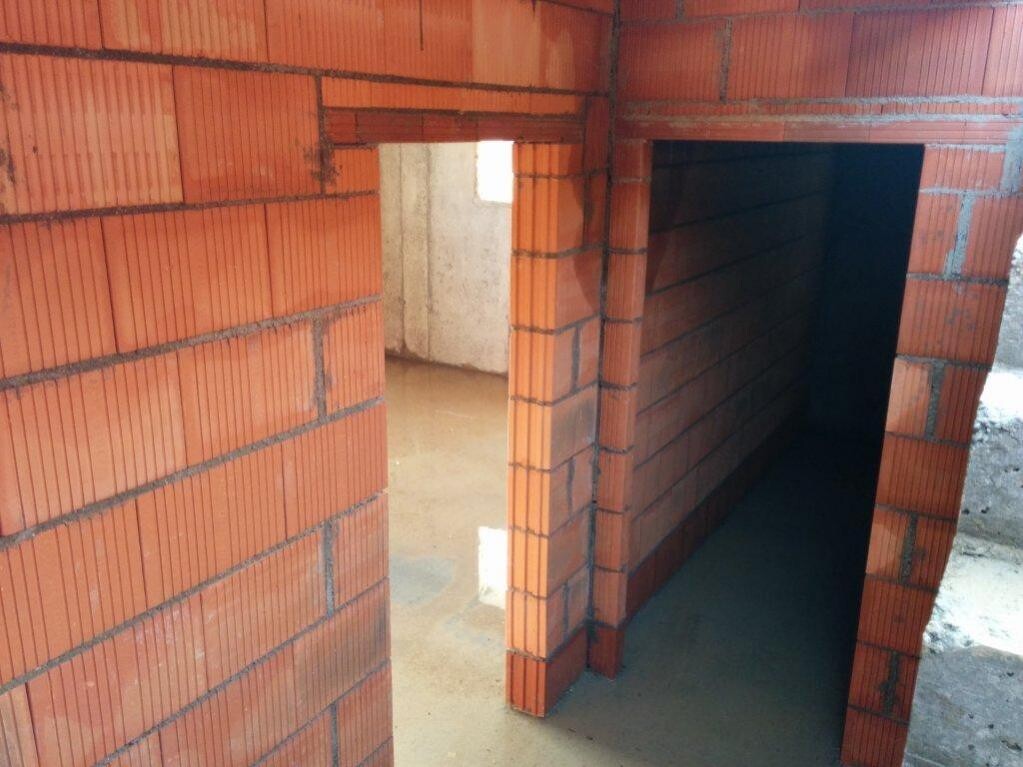 Interior of an unfinished building with red brick walls, open passage to a dark corridor.
