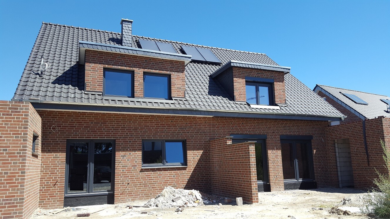 Neues rotes Backsteinhaus mit Dachgauben, Solaranlage und Bauplatz mit Schutt.