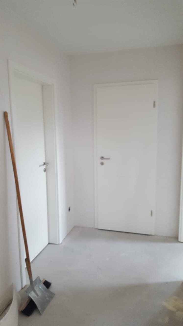Flur in renoviertem Haus, zwei weiße Türen, Besen und Kehrschaufel am Boden.