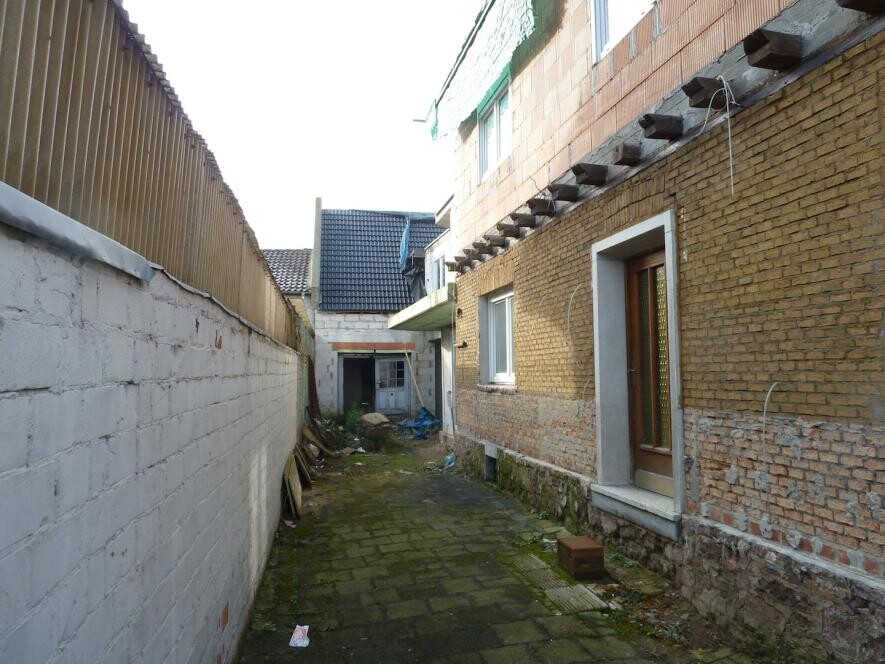 Enger Hinterhof zwischen Ziegelhäusern, gepflasterter Weg, Baugerümpel und Tür zum Haus