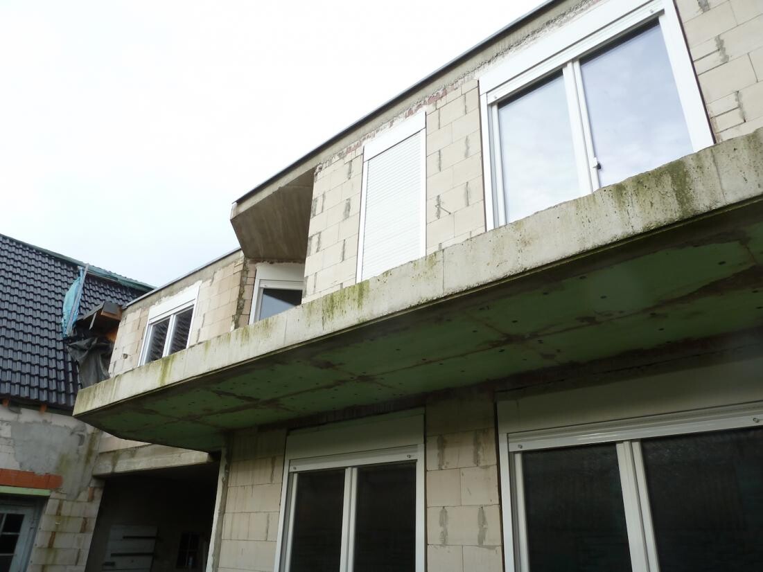 Außenansicht eines unfertigen Gebäudes mit Balkon und Moos am Balkonunterstand
