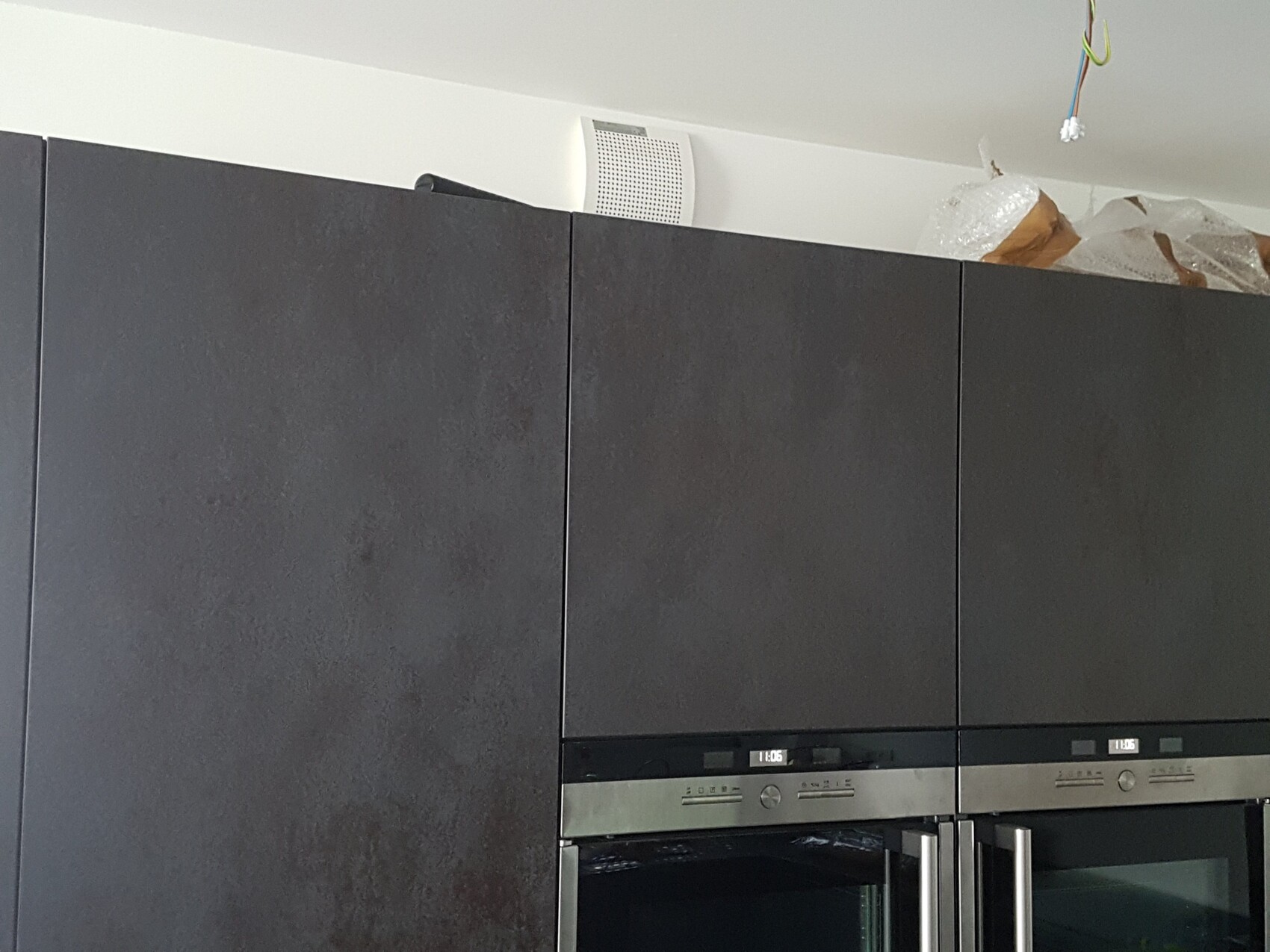Modern kitchen with dark cabinets and two built-in ovens; visible wiring on the ceiling.