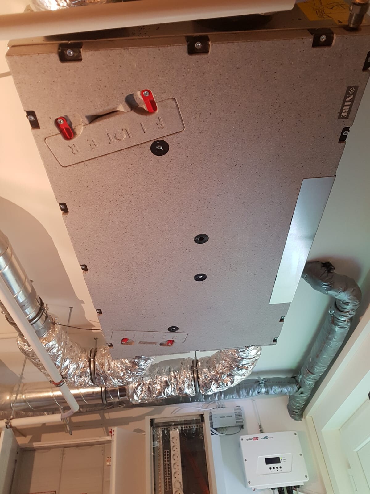 Basement room with building services: insulated air ducts, pipes, and distribution cabinet.