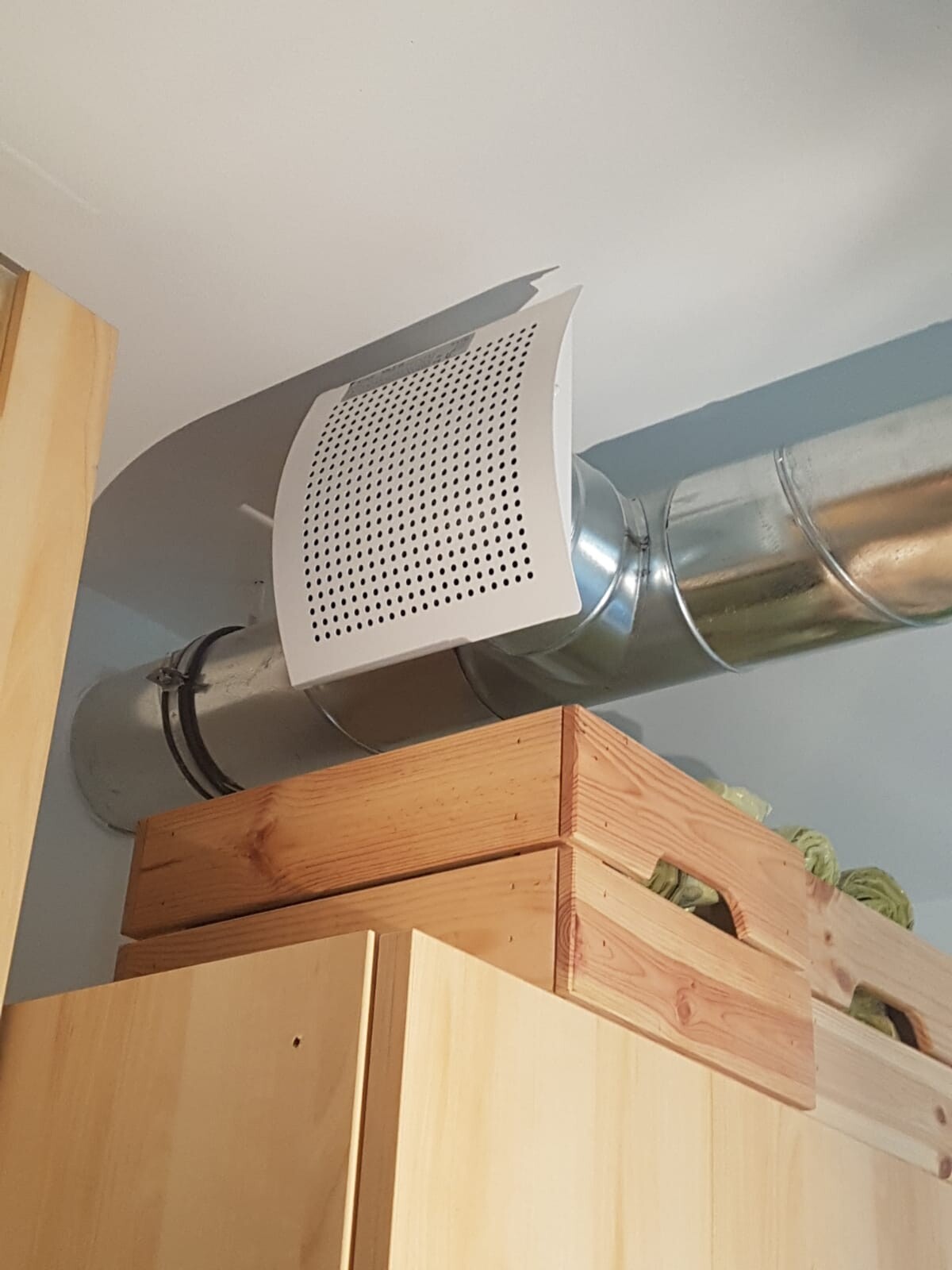 Metal air duct with perforated cover above wooden furniture in basement room