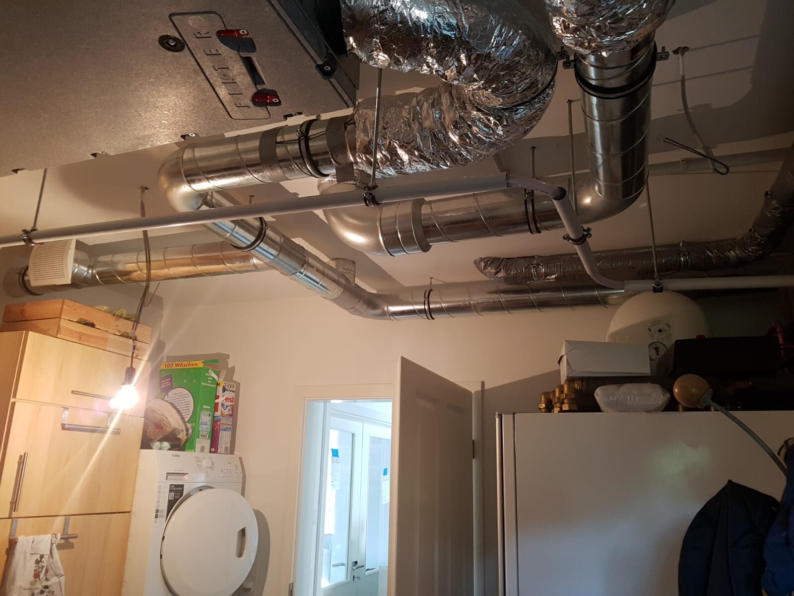 Basement room with visible stainless steel ventilation ducts, piping and washing machine