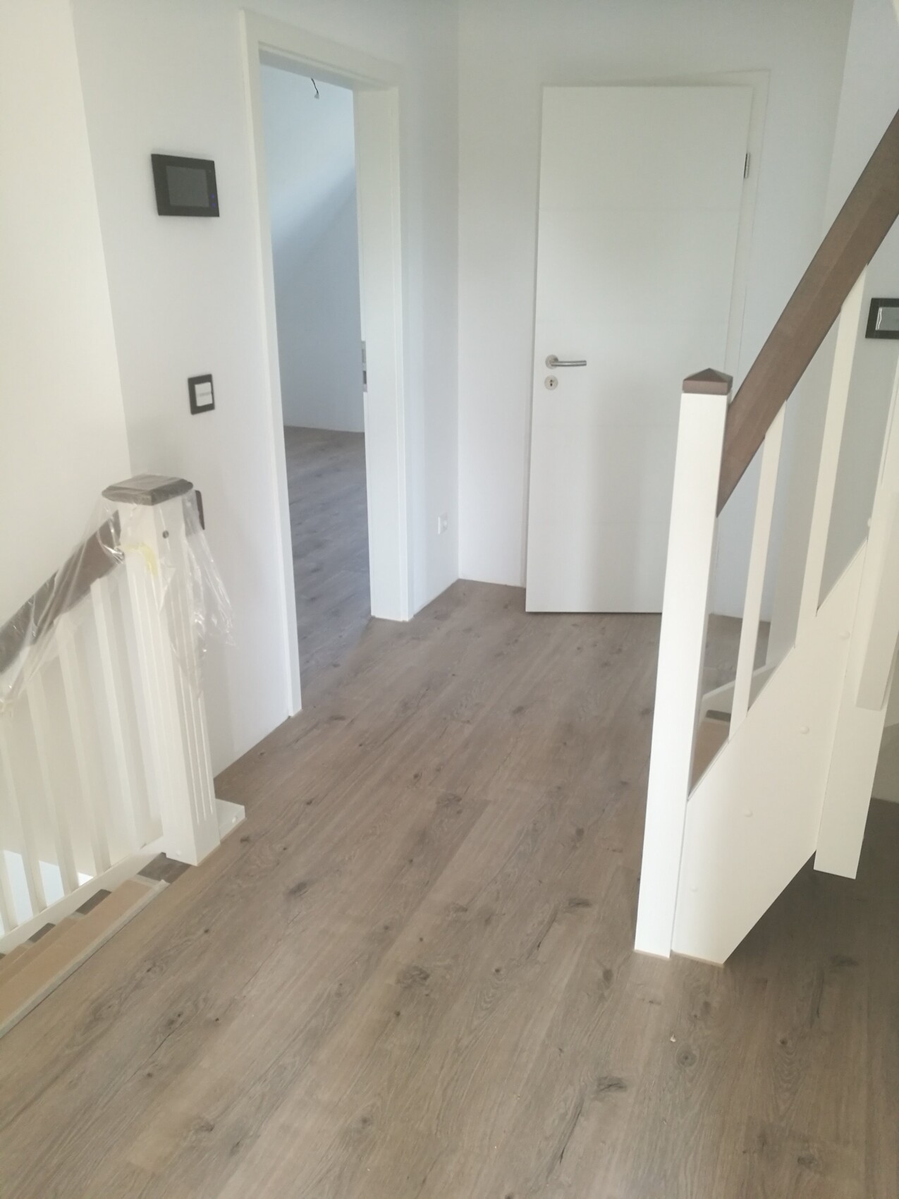 Bright hallway with wooden floor, stairs on the right, open door to the adjacent room.