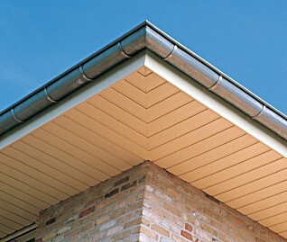 Close-up of a roof edge with gutter, roof overhang and brick wall against blue sky