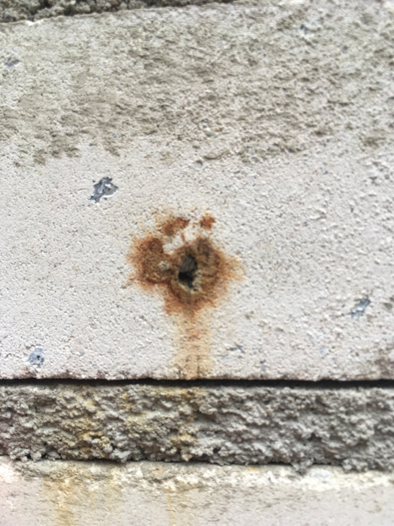 Concrete wall with small hole and rusty discolorations, moisture marks visible