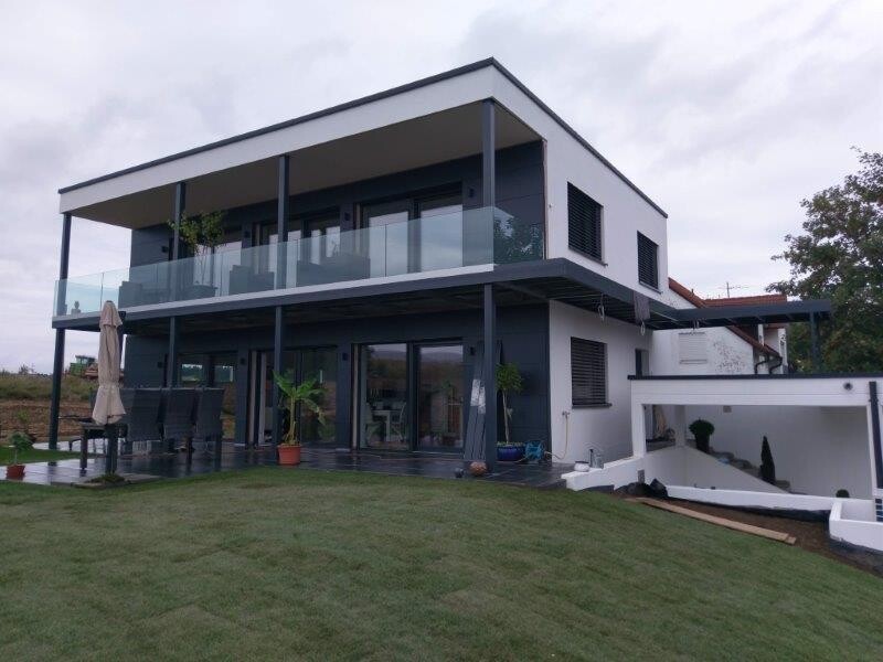 Ein modernes zweistöckiges Haus mit Balkon, Glasgeländer, Terrasse und Garten.