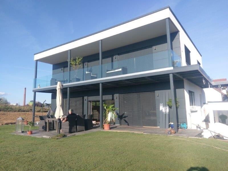 Moderne zweistöckige Villa mit Glasgeländer, Terrasse und Gartenmöbel
