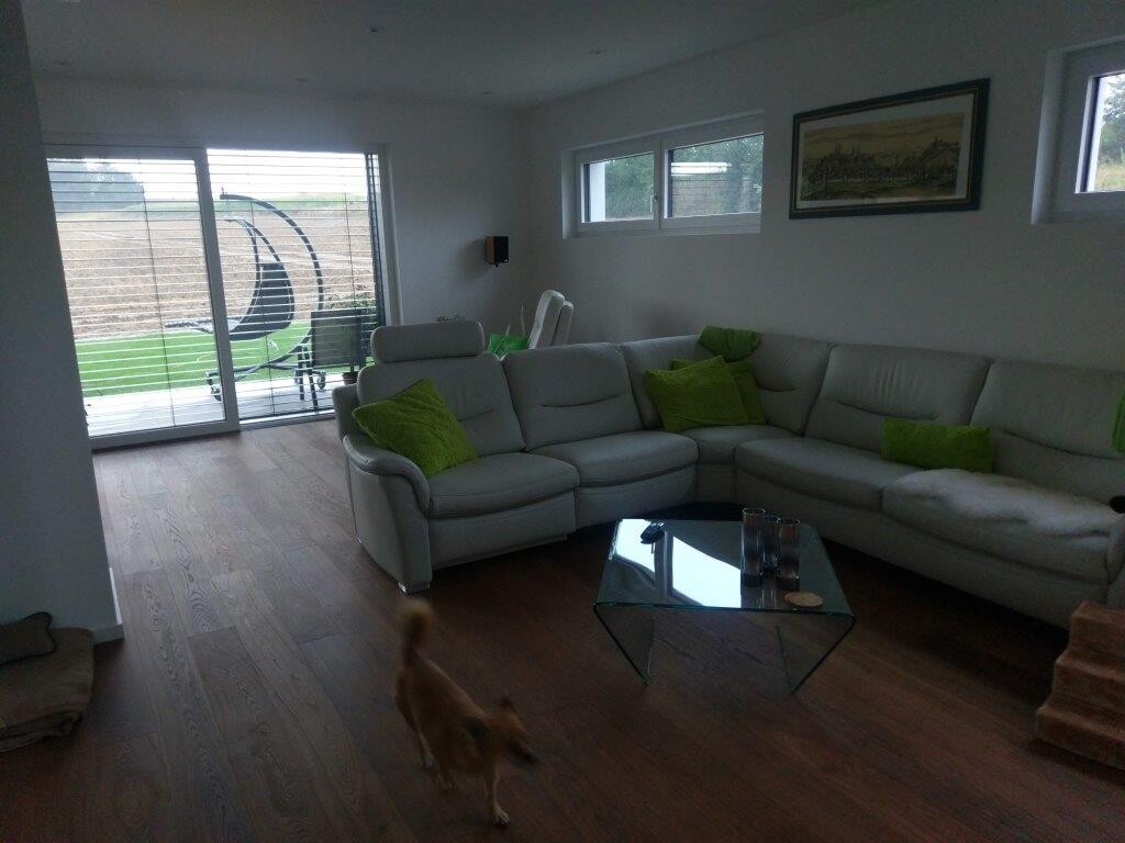 Helles Wohnzimmer mit grauer Eckcouch, Glas-Couchtisch und grünen Kissen