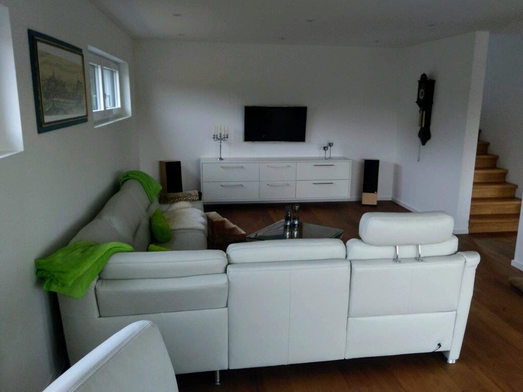 Helles Wohnzimmer mit weißer Ledersofa-Gruppe, TV-Schrank, grüne Decke, Treppe.