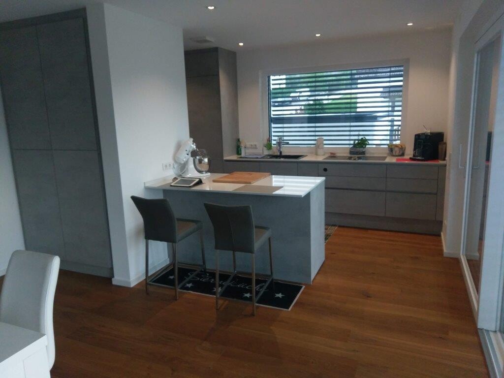 Moderne Küche mit grauen Fronten, Kücheninsel, zwei Barhockern und Holzboden.