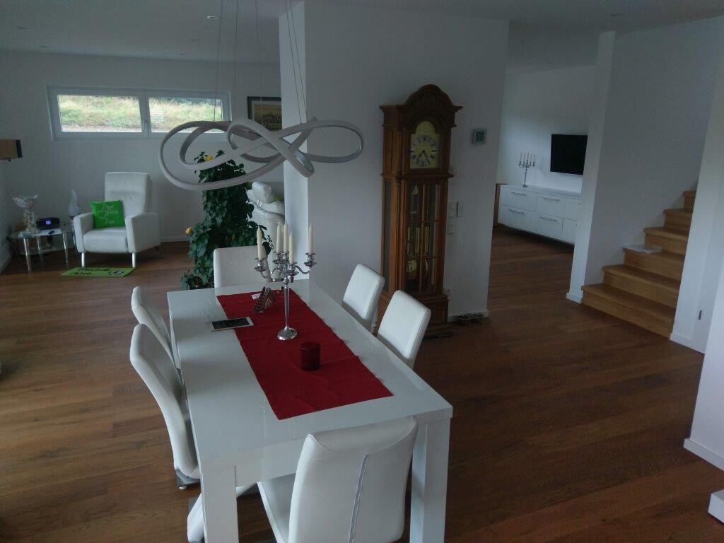 Helles Esszimmer mit weißem Tisch und weißen Stühlen, rotem Läufer, Kerzenleuchter, Standuhr.