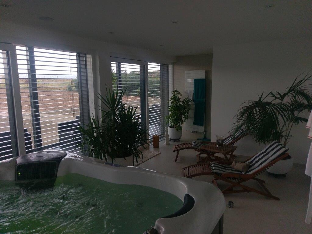 Moderner Innenraum mit Jacuzzi, Lounge-Sesseln, Pflanzen und großen Fenstern.