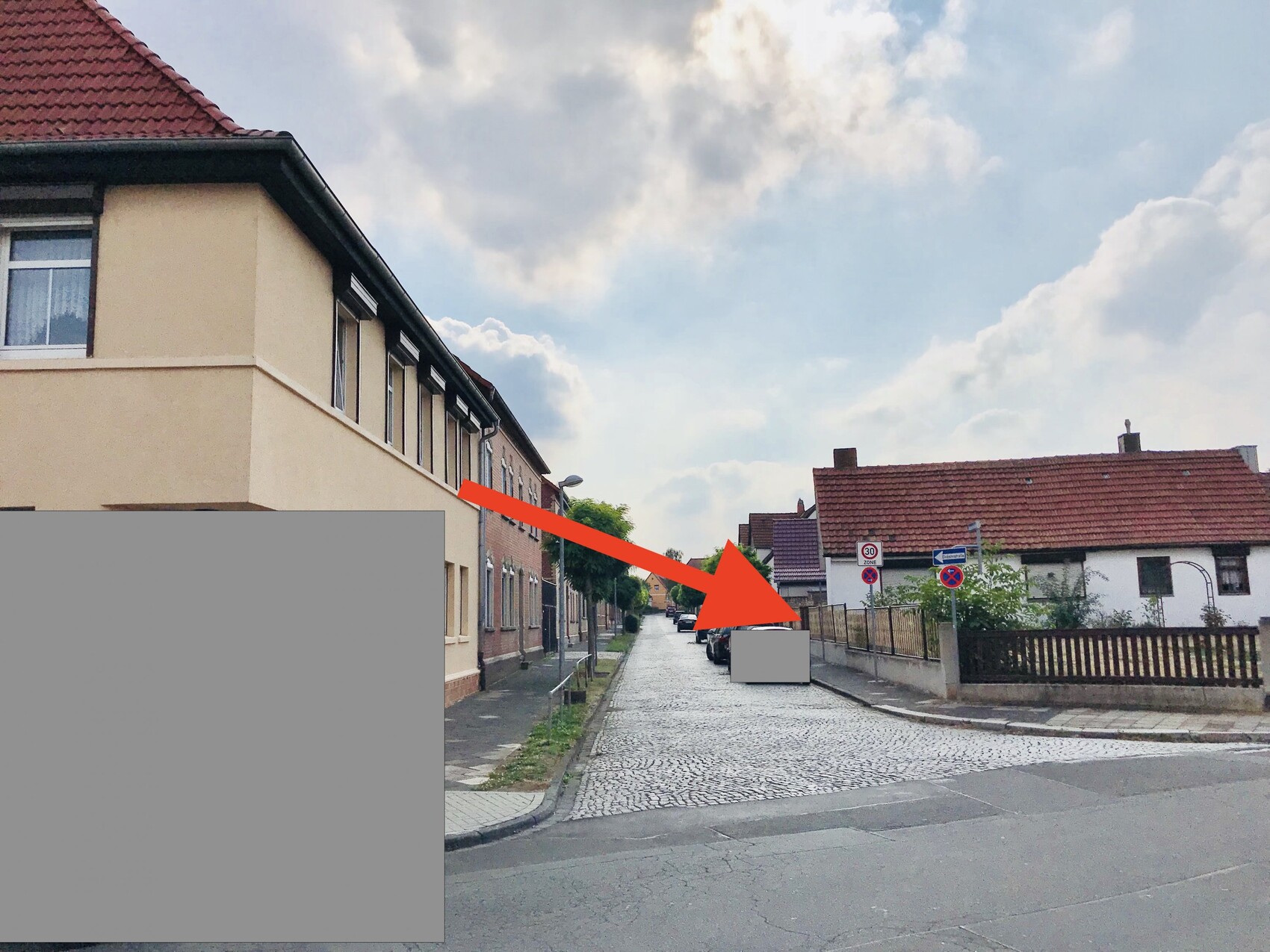 Street view with townhouses on the left, single-family homes on the right, paved street and clouds.