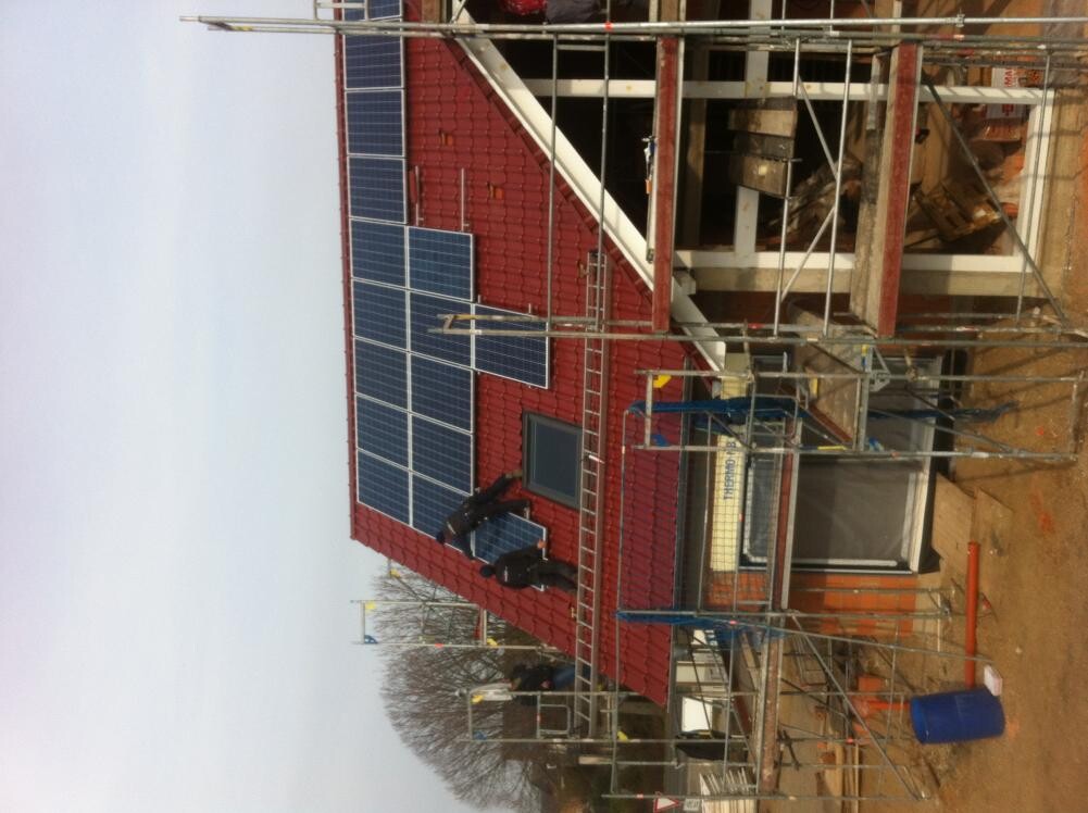 Construction site with red roof, solar panels installed, and scaffolding around the building.