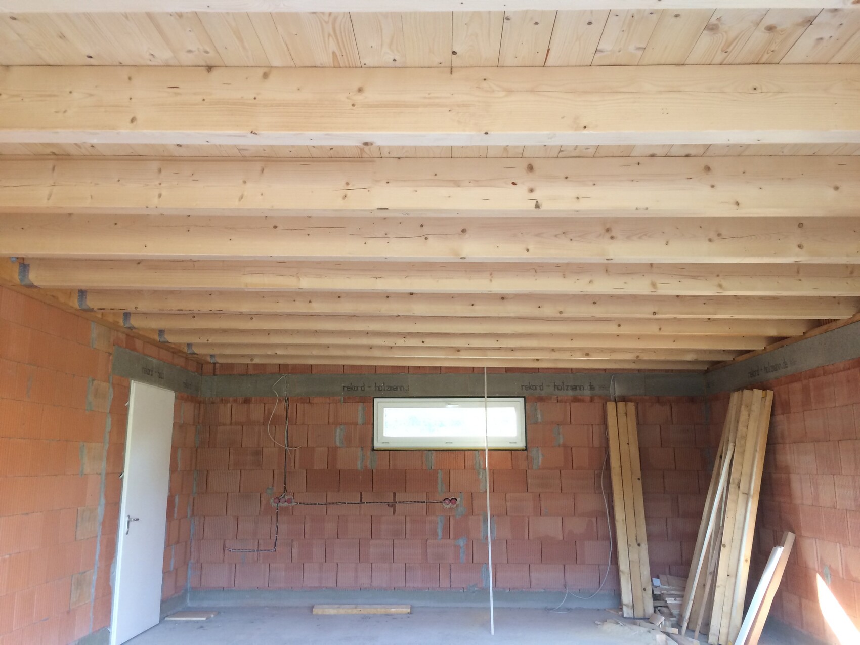 Interior of a construction site: visible timber beam ceiling, brick walls, windows, stack of wood.