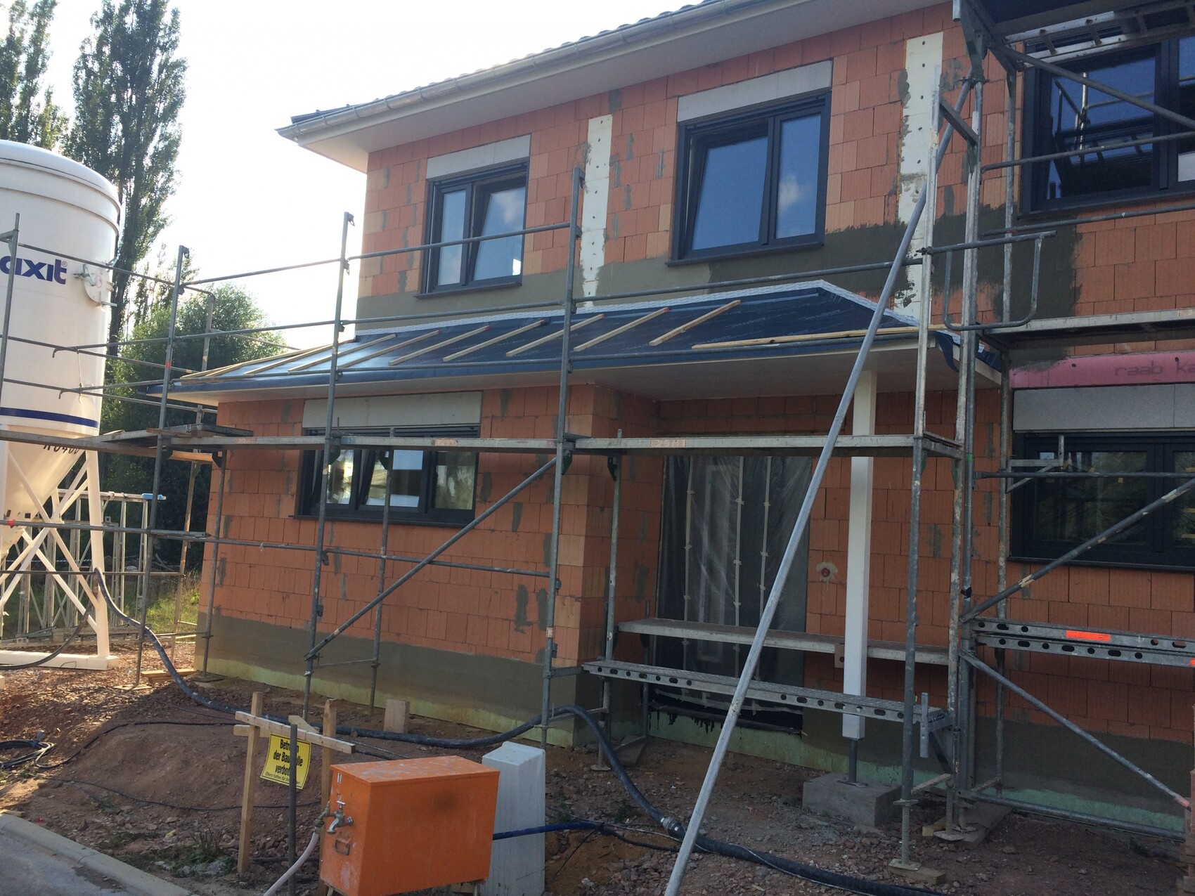 Two-story house under construction with scaffolding, orange brick façade, and building materials.