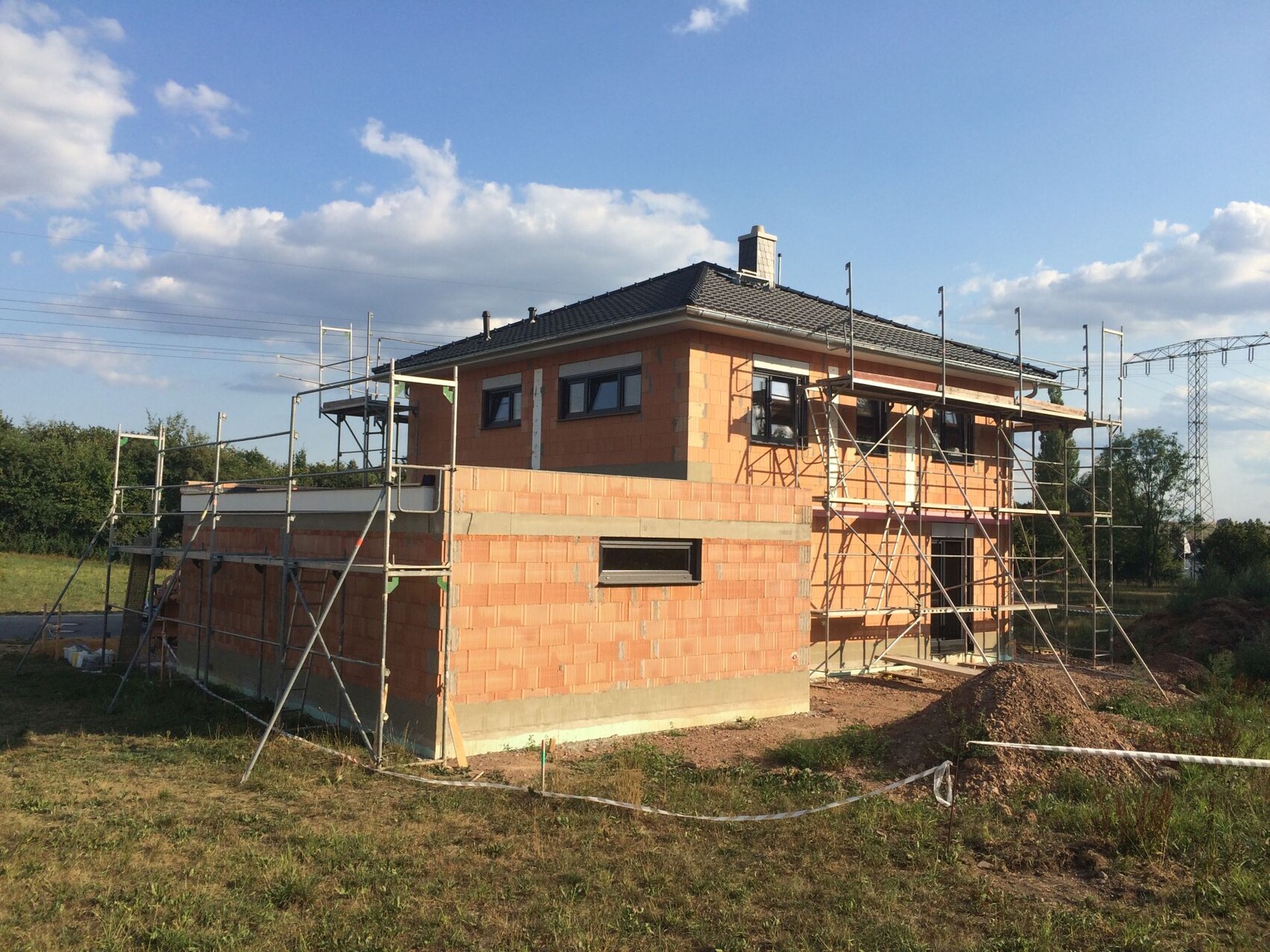 Brick shell construction of a two-story house with scaffolding and roofing work.