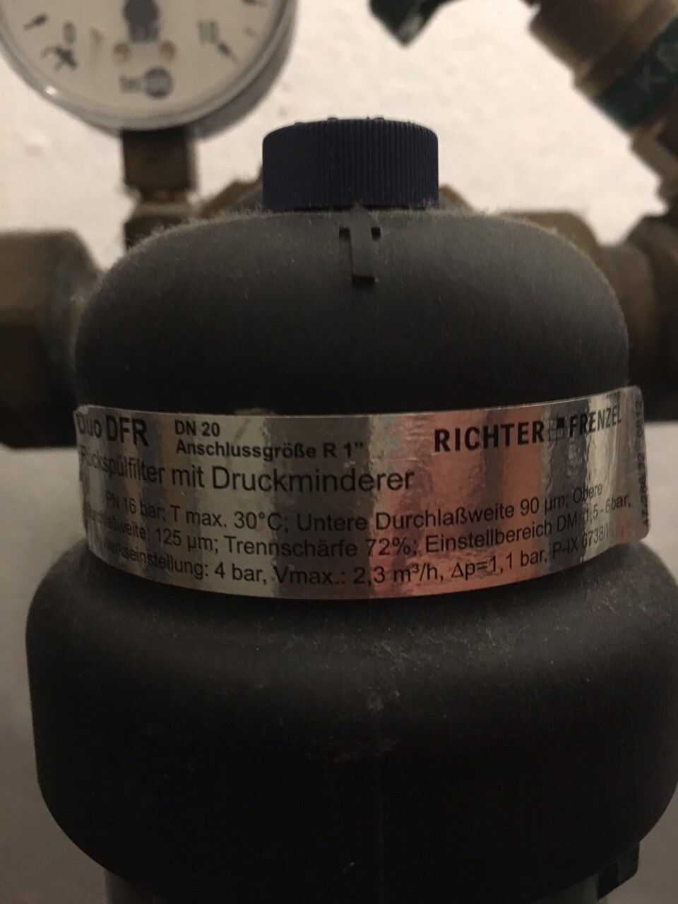 Close-up of a gas pressure regulator (pressure reducer) with metal band label; measurement display in background
