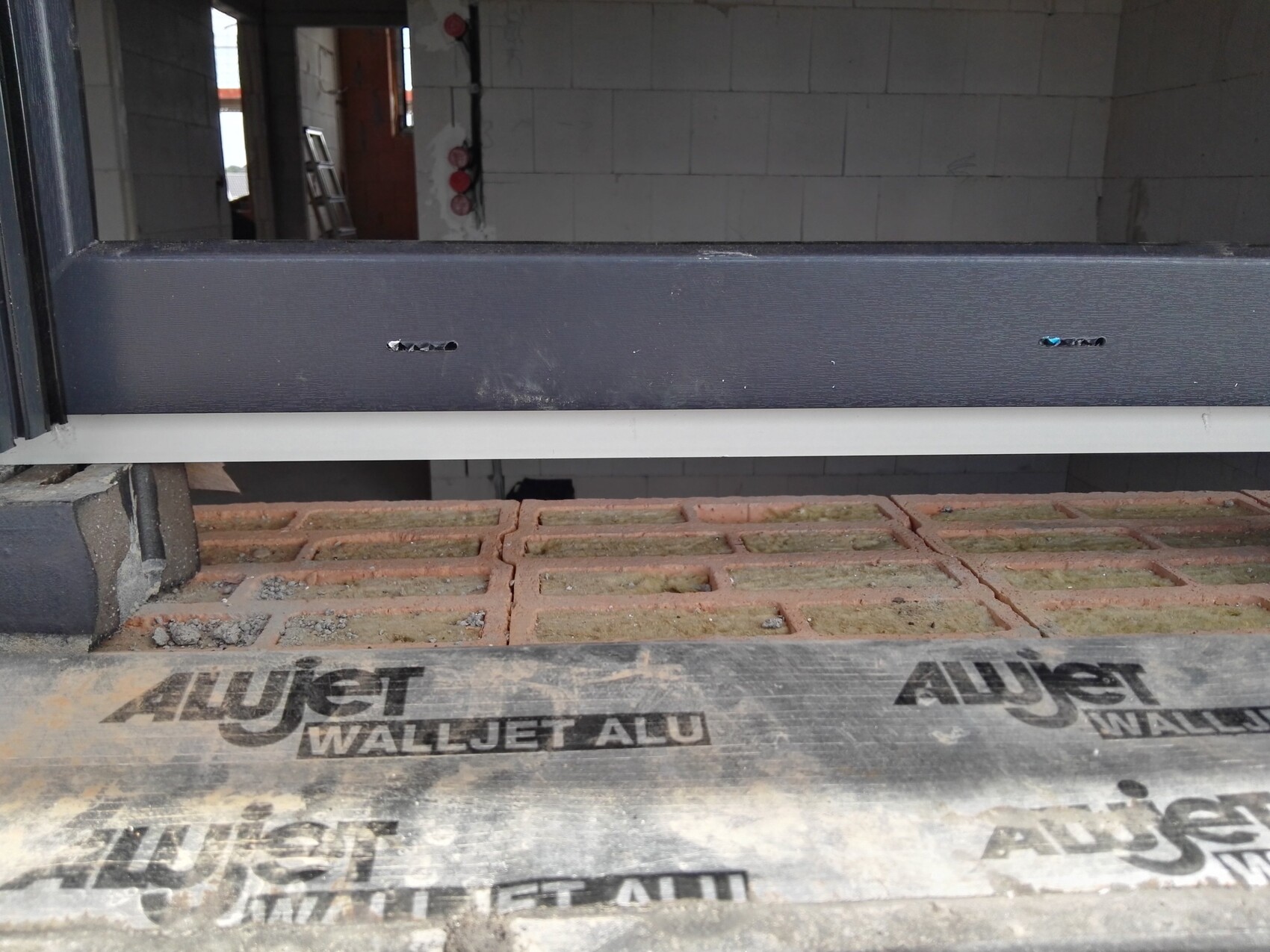 View of a construction site: dark metal beam above a red brick floor inside.