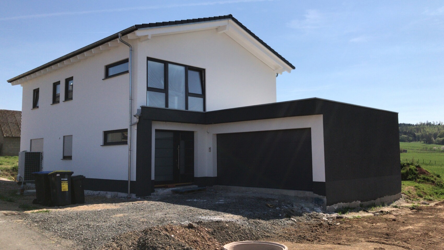 Modern white house with black accents and large attached garage in front of green field.