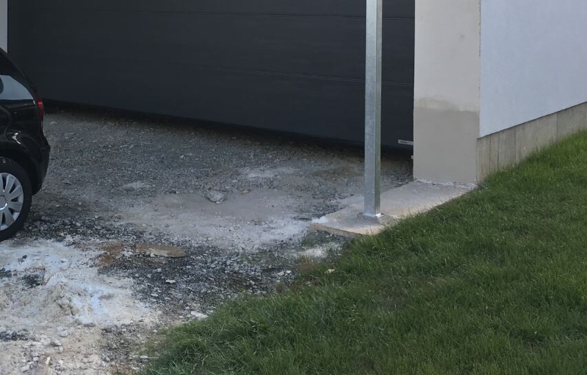 Construction site in front of house: foundation, gravel base, grass edge, metal support, parked car