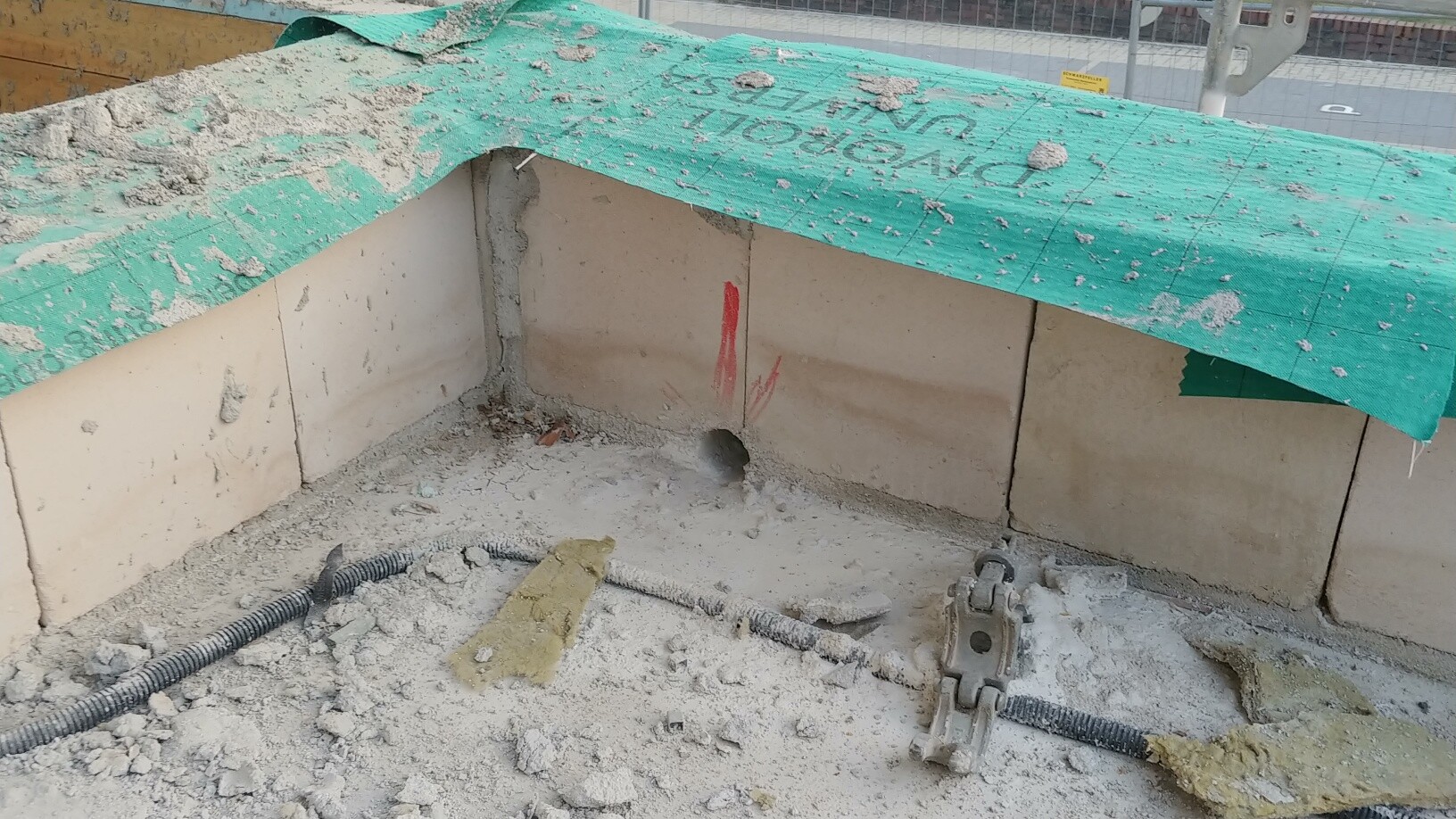 Baustelle mit Betonfundament, grüne Abdeckung, Kabel und Schutt