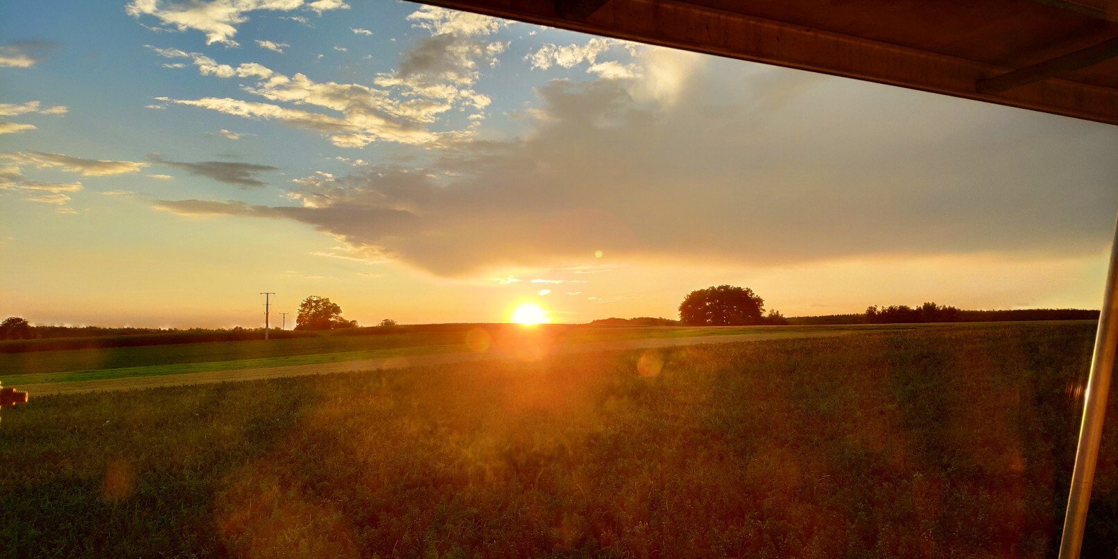 Sunset over wide fields, view from a terrace onto open landscape with trees.