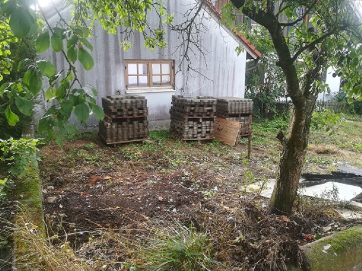 Garden area in front of small house with stacked stones and wooden pallets