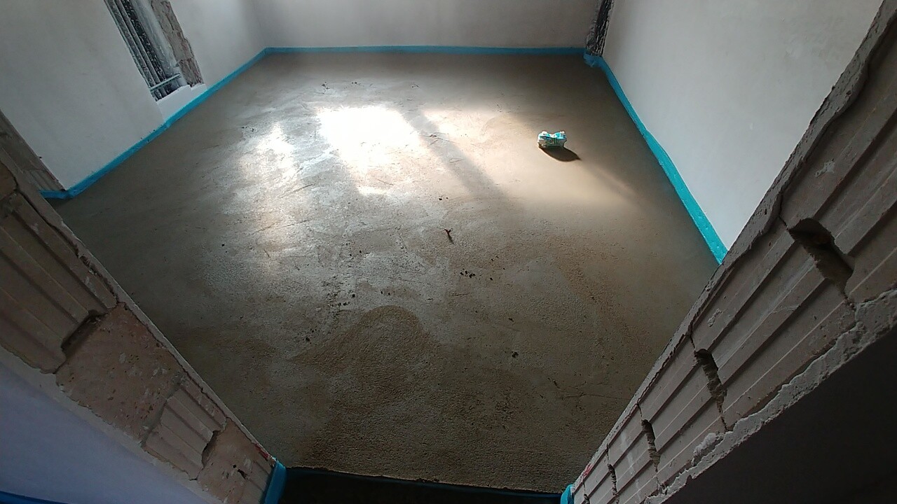 Rohbau-Raum mit Betonboden, blaue Randkanten und unfertige Innenraumkonstruktion