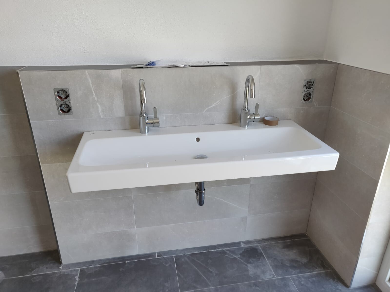 Washbasin with two faucets in a bathroom under renovation with gray tiles