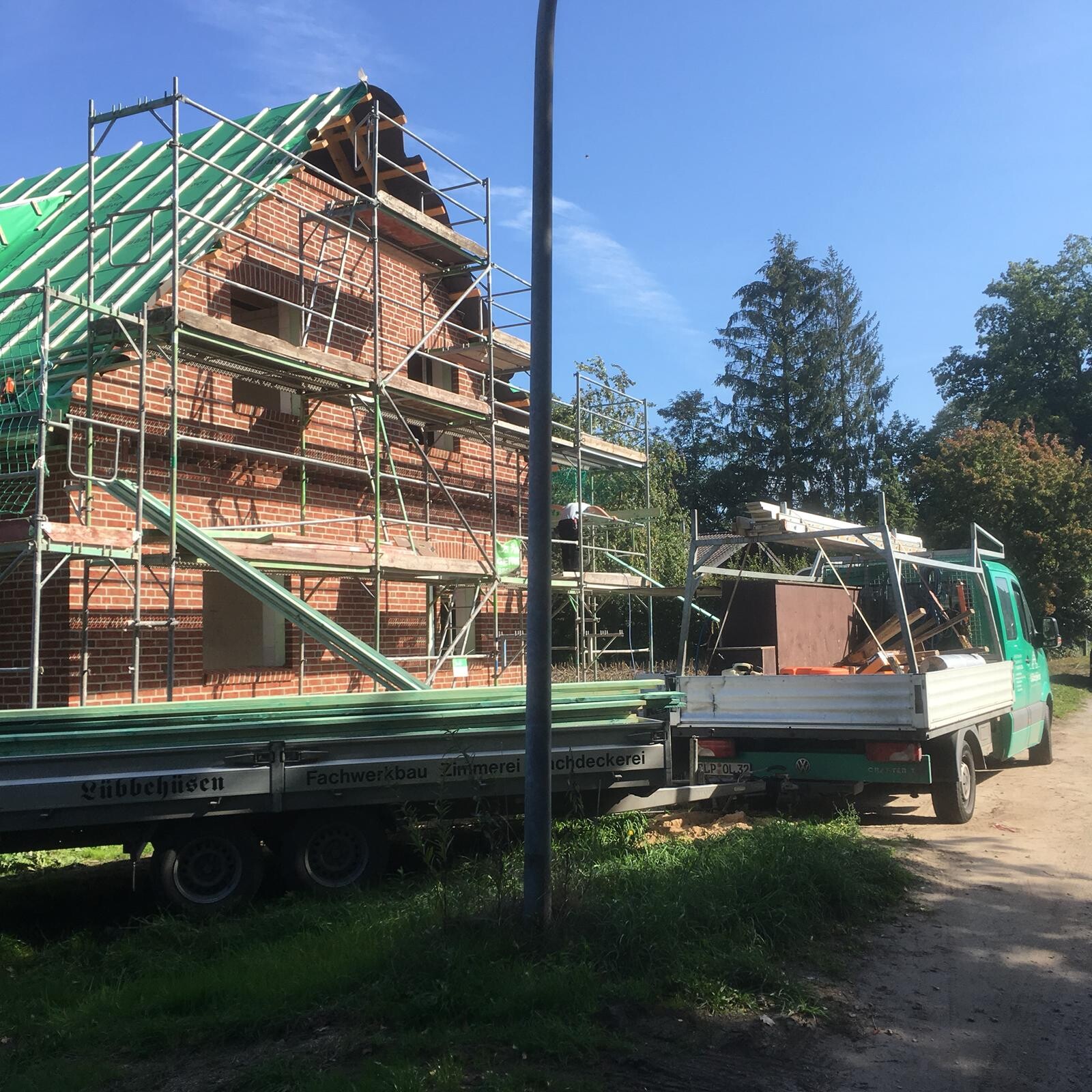 Construction site of a brick house with scaffolding, green roof, and construction truck.