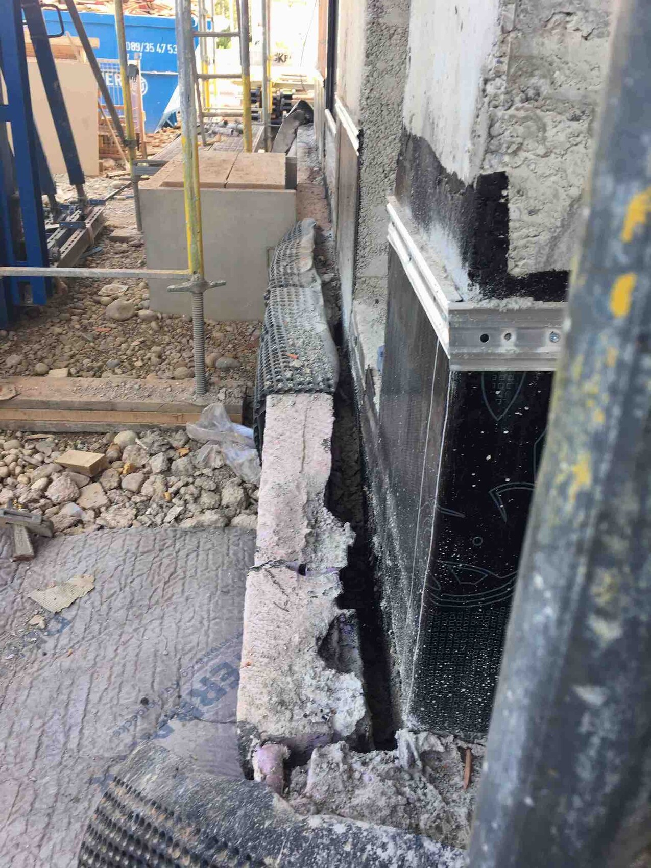 Construction site: open foundation, concrete blocks, debris, and scaffolding next to the wall