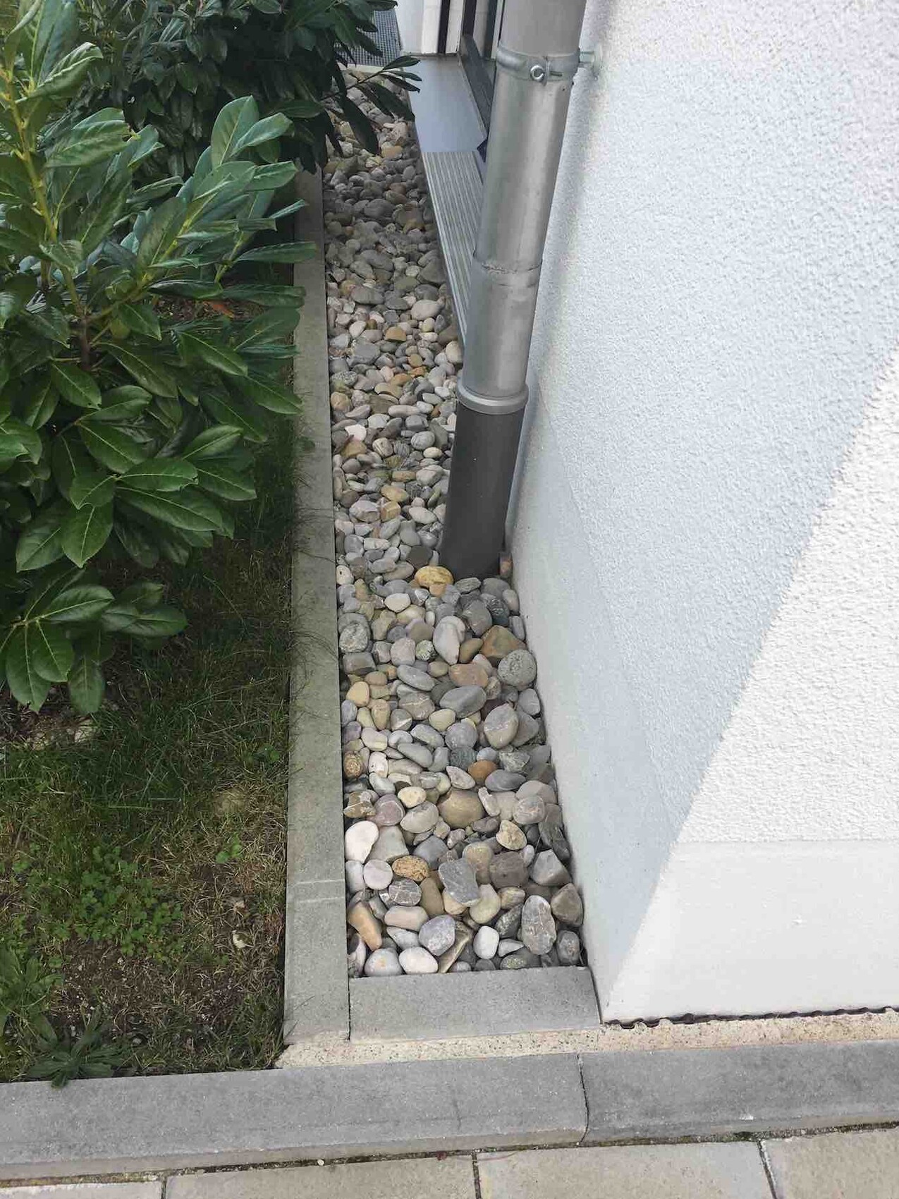 Exterior view of a building with a gravel path beside the wall and downpipe.