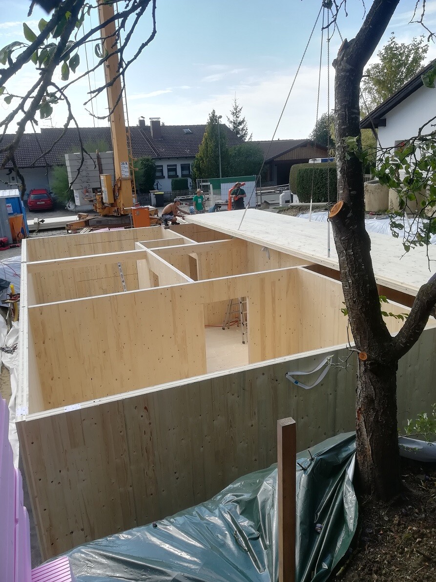 Construction site: Timber frame house under construction, workers working, crane in the background.