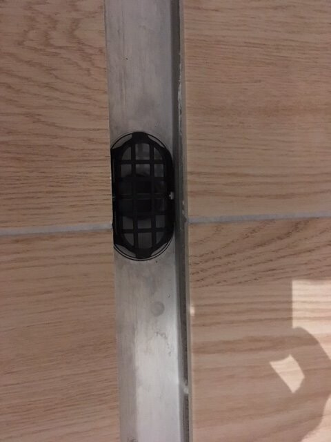Black floor vent grille in metal channel between bathroom floor tiles