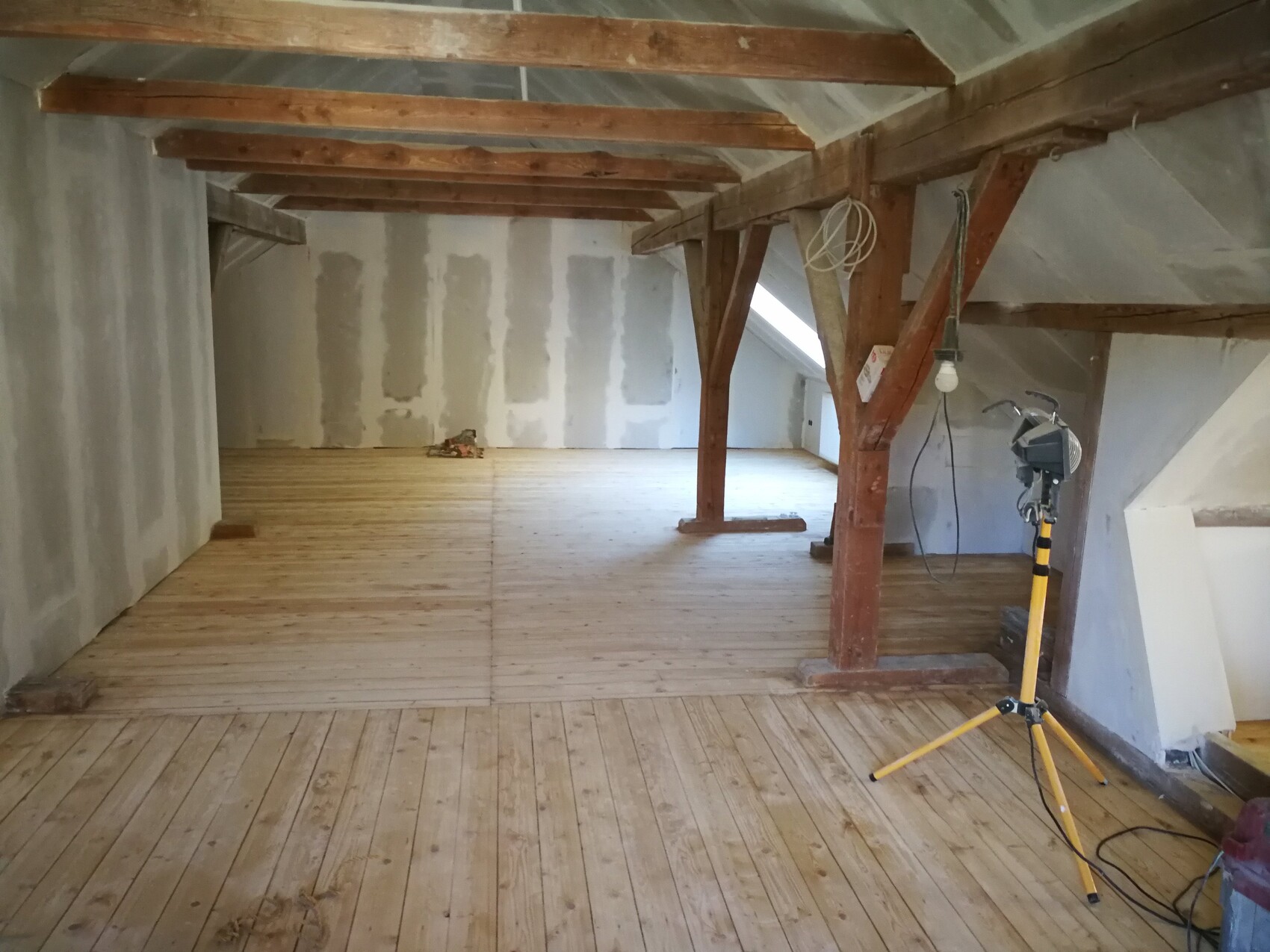 Dachboden im Rohbau mit sichtbaren Holzbalken, Holzboden und Bauleuchte