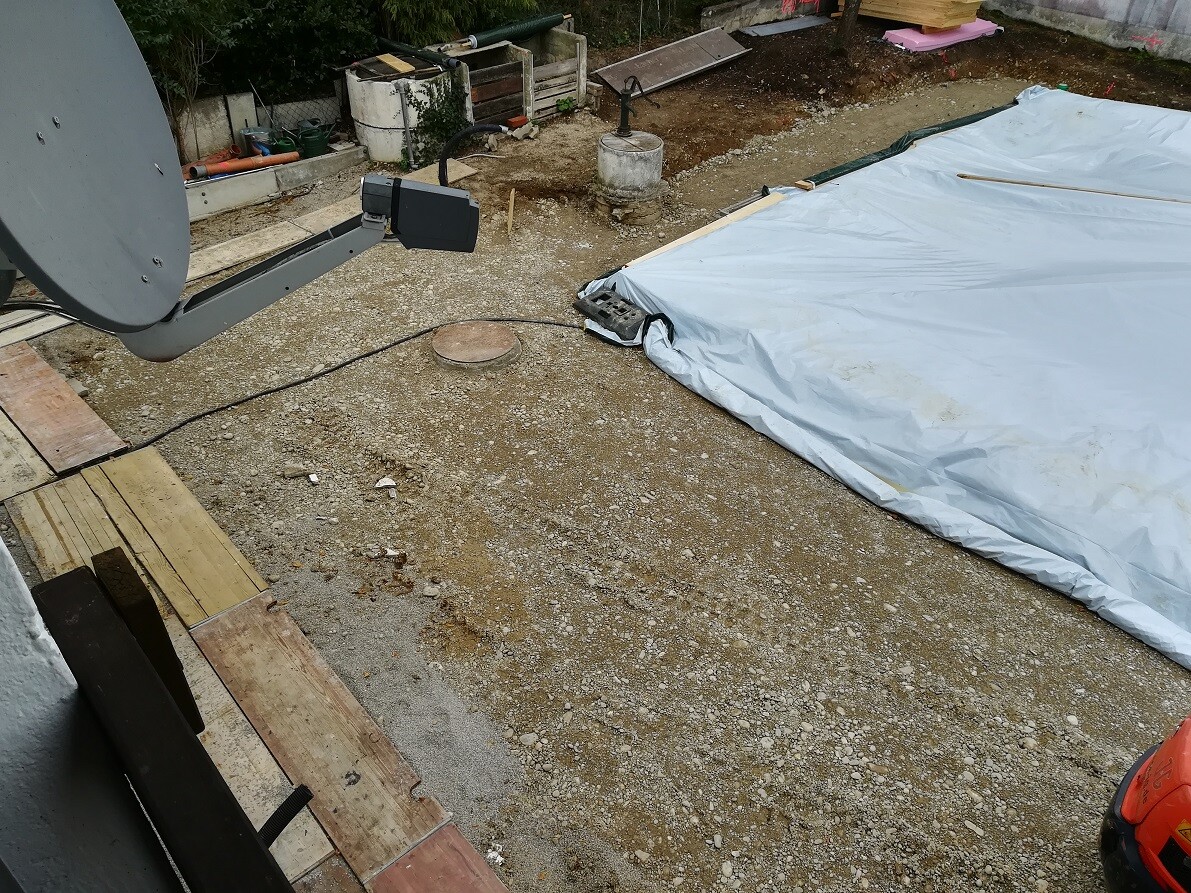 Outdoor construction site with a tarpaulin, building materials, and excavated soil.