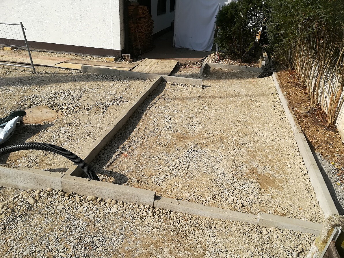 Construction site with foundation framework, gravel base, concrete gutters, and access to the house