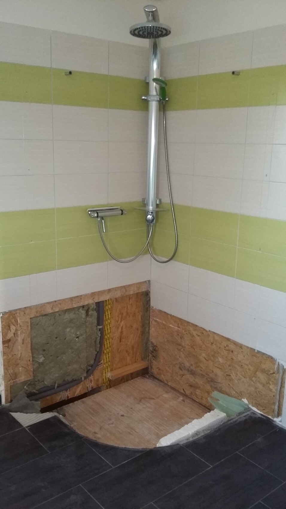Duschbereich im Bau: Regenkopf, Handbrause, grün-weiße Fliesen, offener Boden.