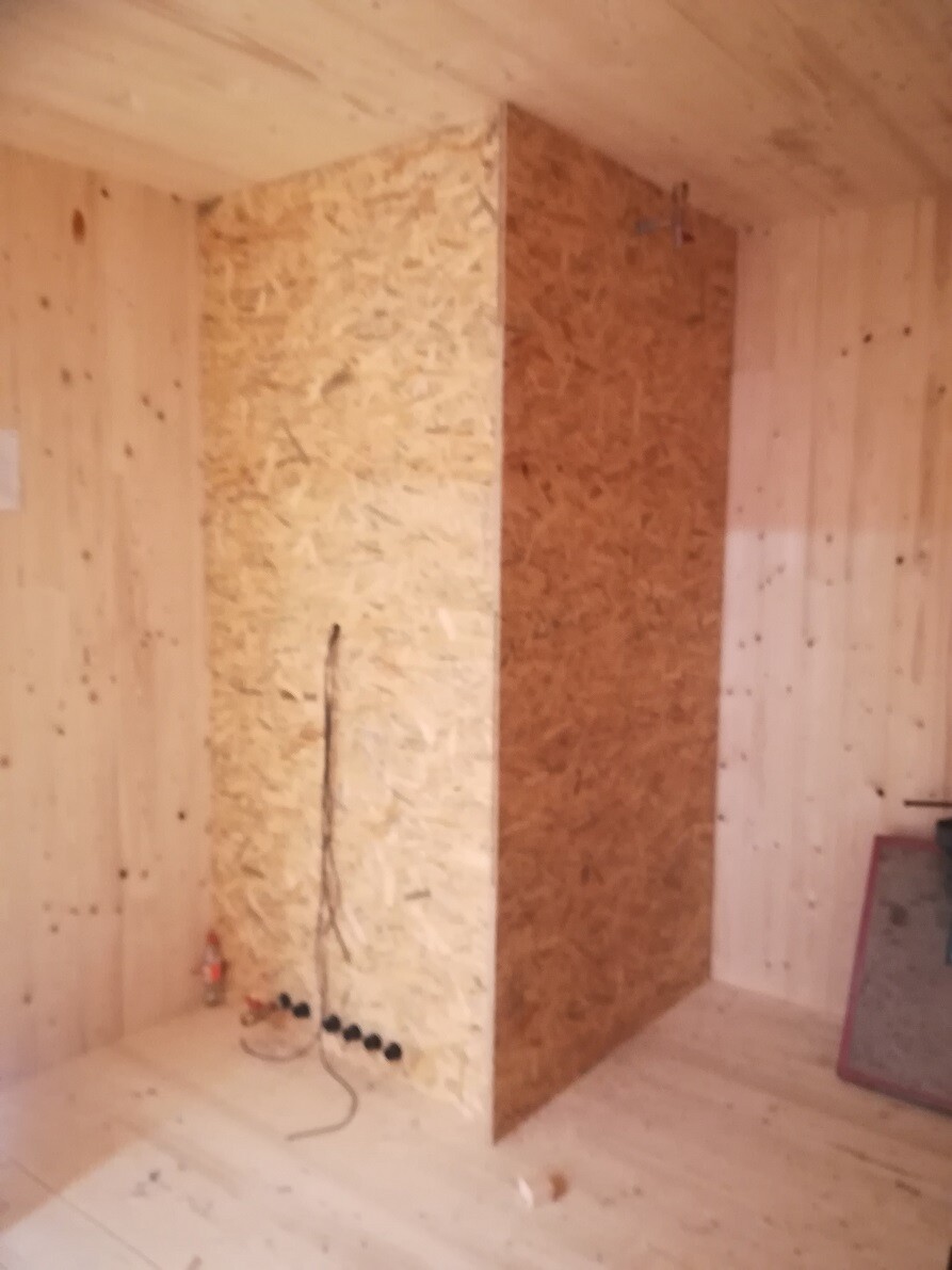 Interior with OSB walls and wood paneling, visible electrical installations.