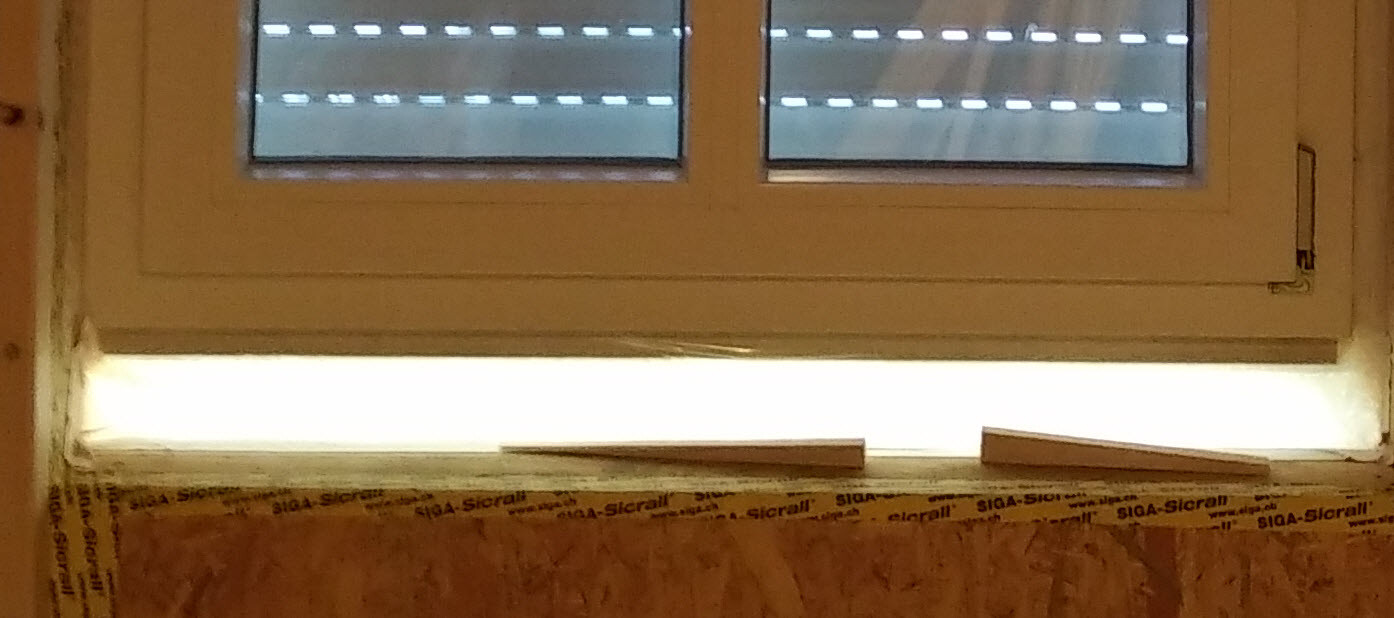 Window under construction with open blinds, construction debris, and sealing tape on the frame.