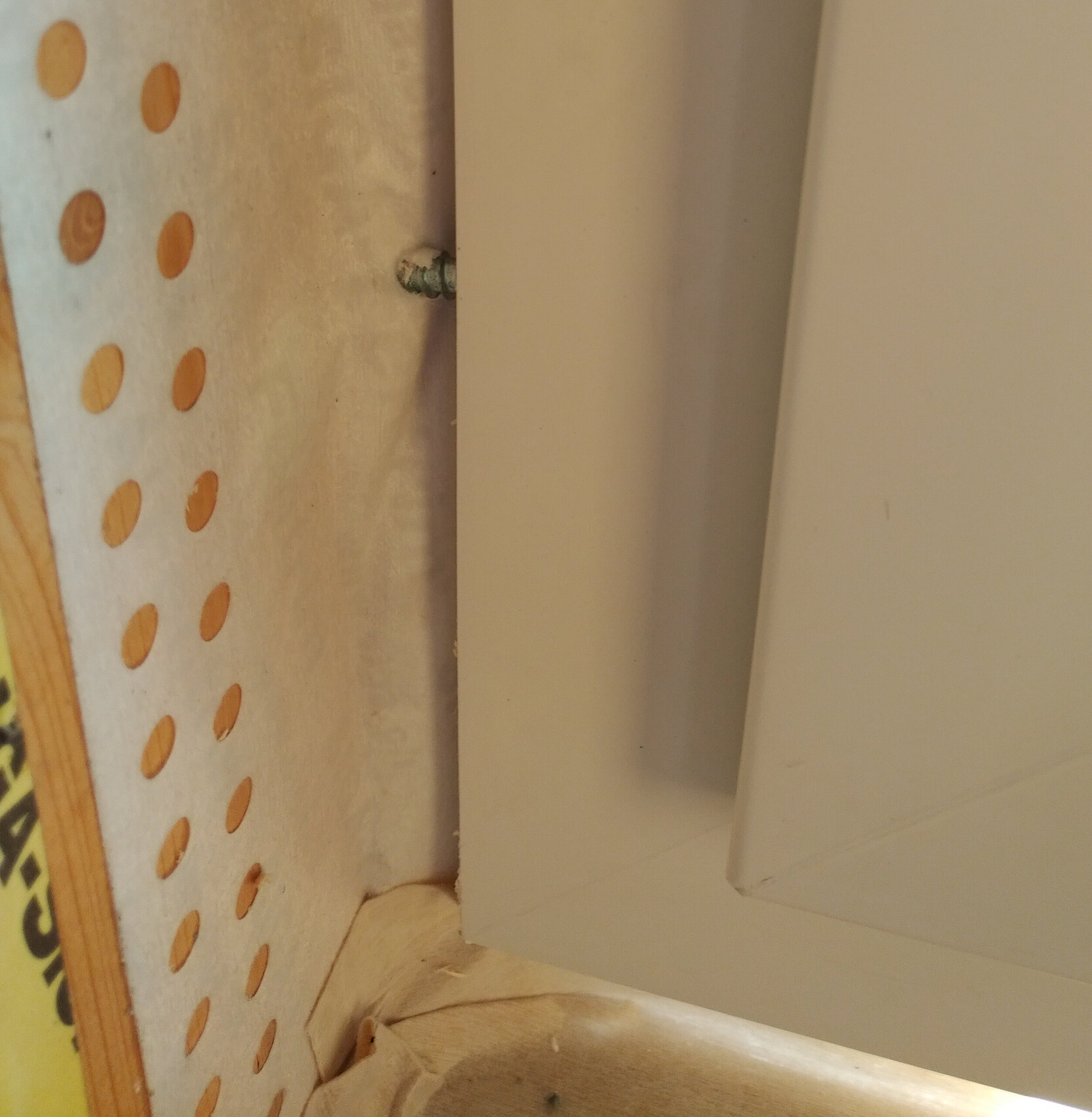Close-up of a white frame next to pegboard perforated panel in interior construction.
