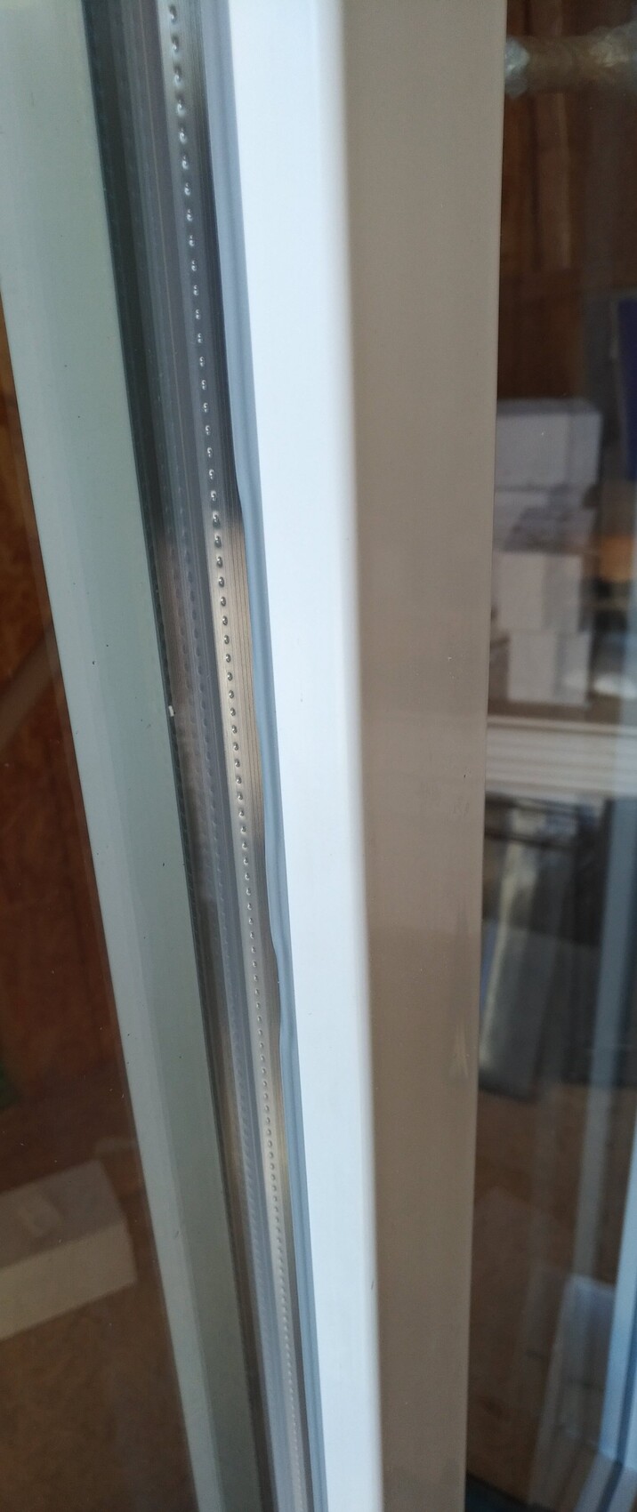 Close-up of a window frame with metal strip and glass front, interior visible.