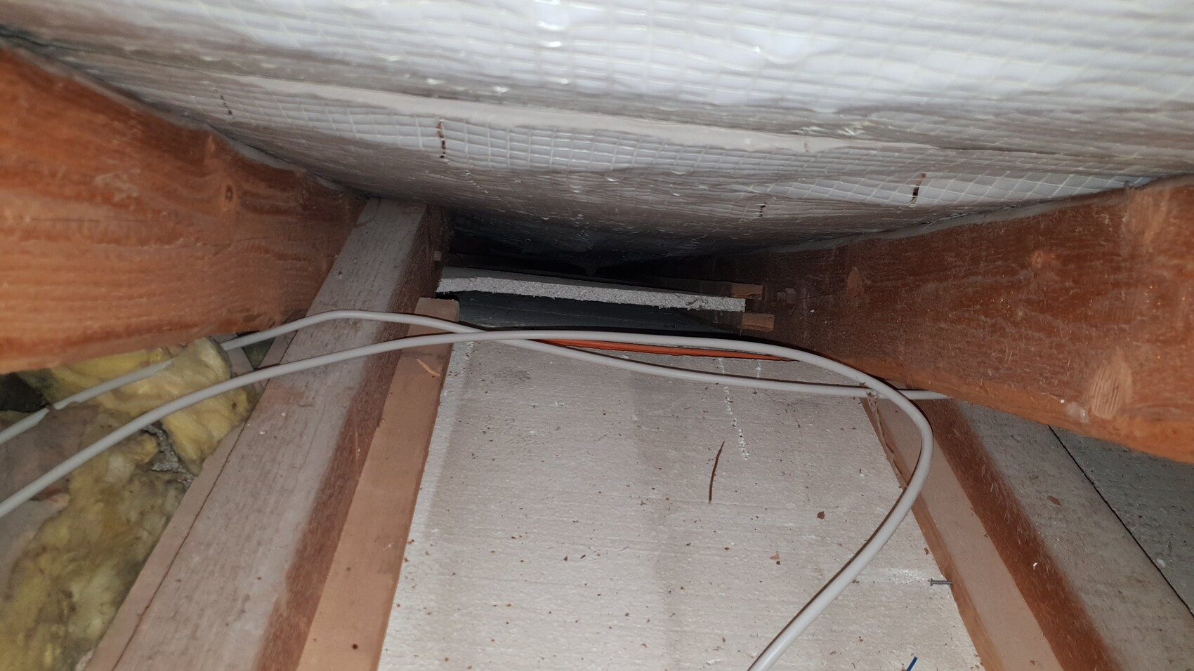 Attic with wooden beams, insulation and visible cables
