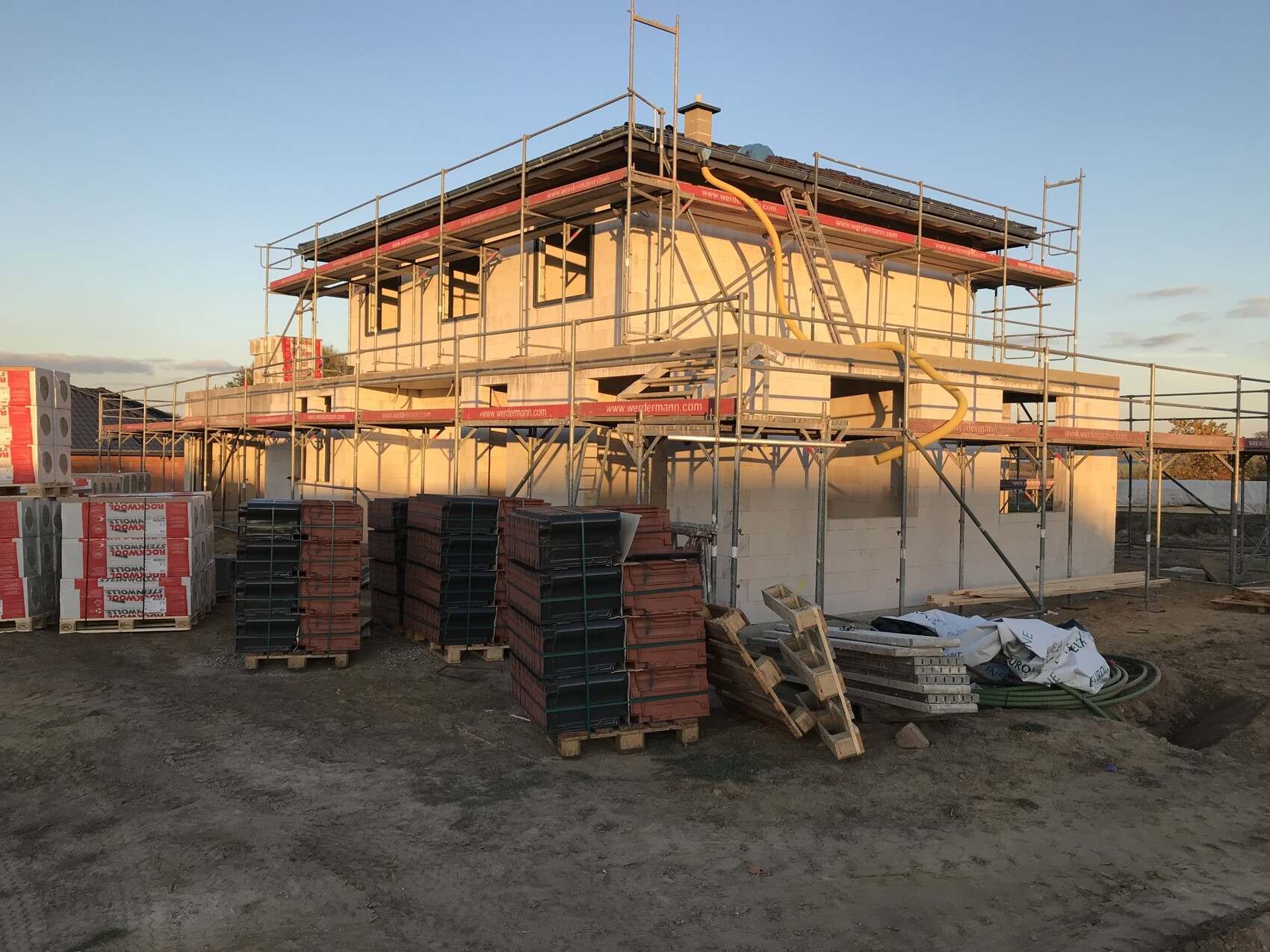 Baustelle mit Gerüst und unfertigem Haus im Rohbau, Baumaterialien auf dem Gelände