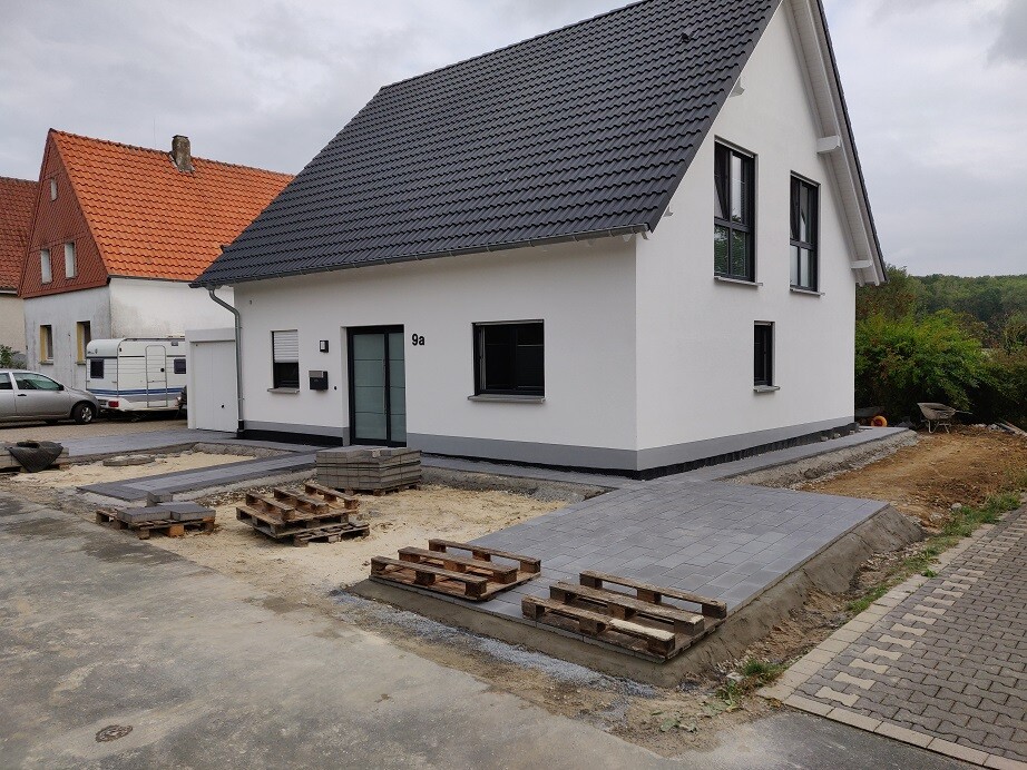 Modernes Einfamilienhaus mit weißer Fassade, dunklem Dach, Vorplatz aus Pflastersteinen